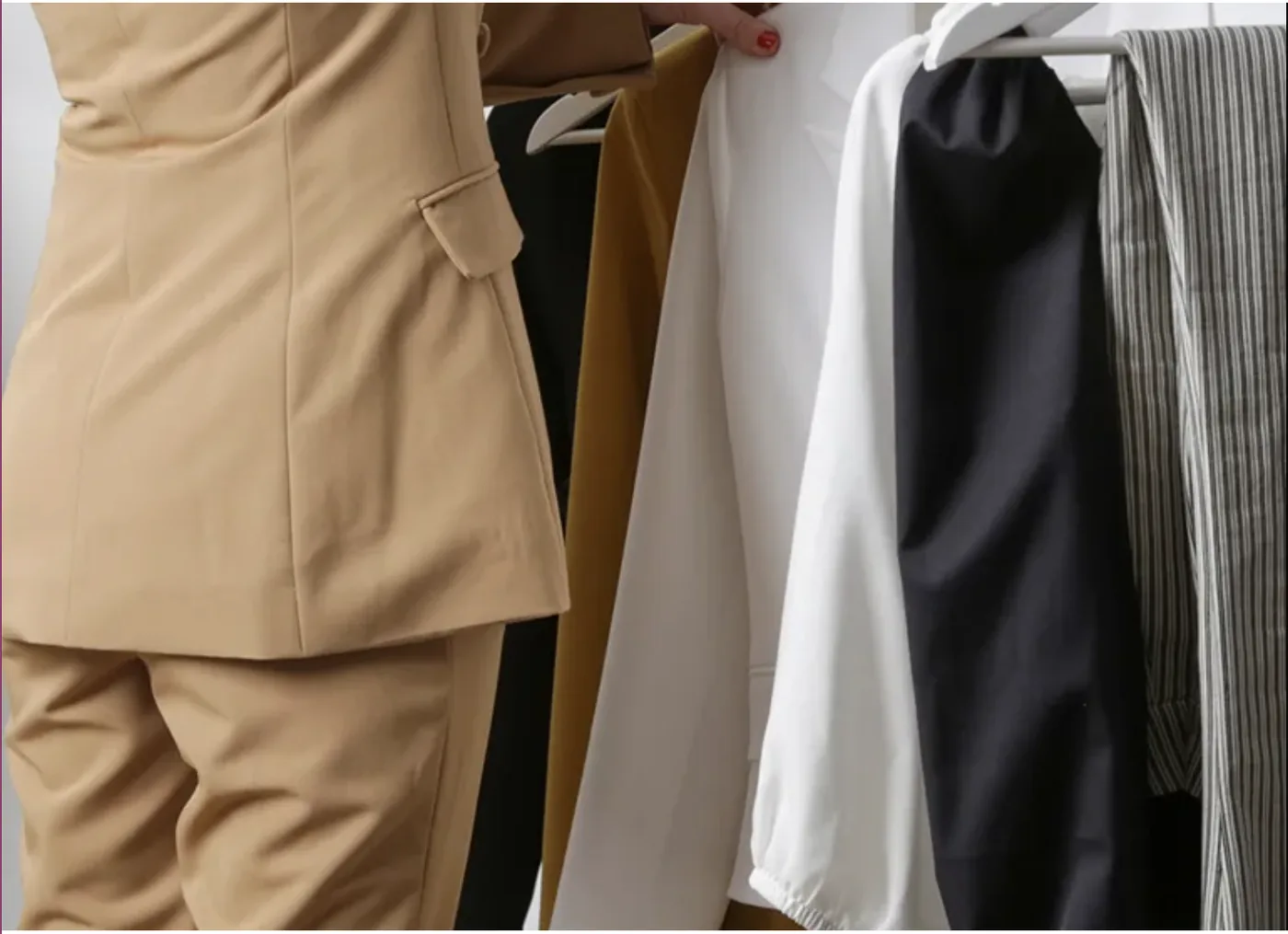 Prendas de un fondo de armario colgadas en fila: traje camel, pantalón blanco, blusa negra y camisa de rayas